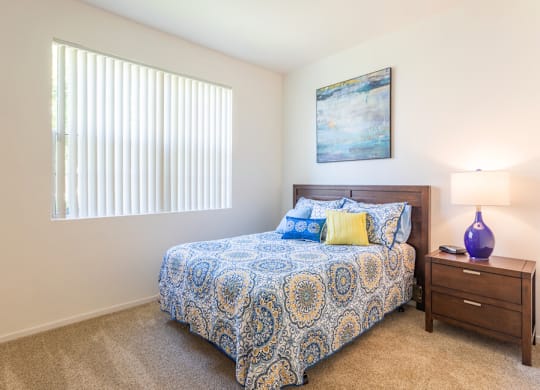 A bedroom with a bed, nightstand, and a painting on the wall at Palm Court Apartments, Salinas