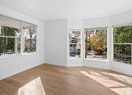 A sunny room with a wooden floor and three windows showing trees and a street at Westmont Place Townhomes Apartments, Santa Cruz, CA, 95060