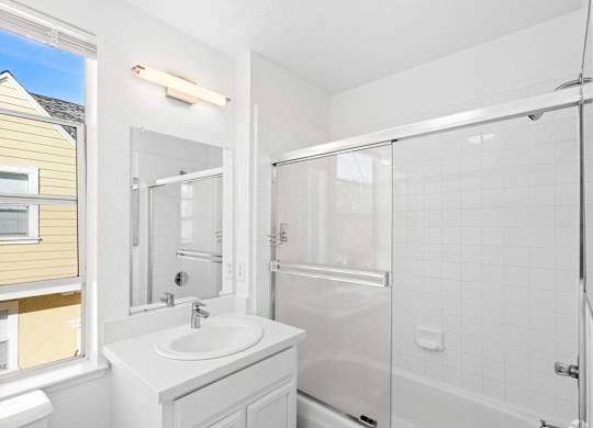 A white bathroom with a sink, mirror, and shower at Westmont Place Townhomes Apartments, Santa Cruz, California