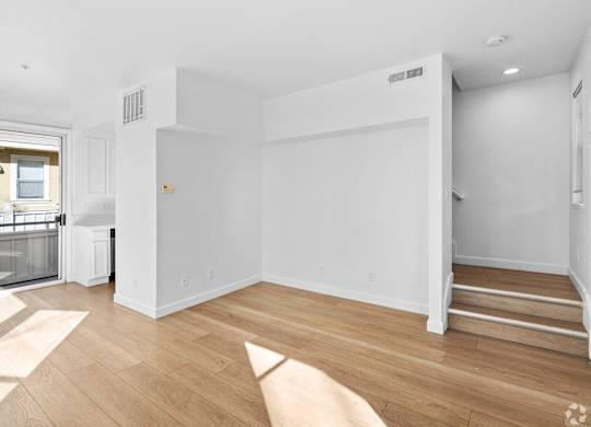 A white room with wooden flooring and a staircase on the right side at Westmont Place Townhomes Apartments, Santa Cruz, 95060