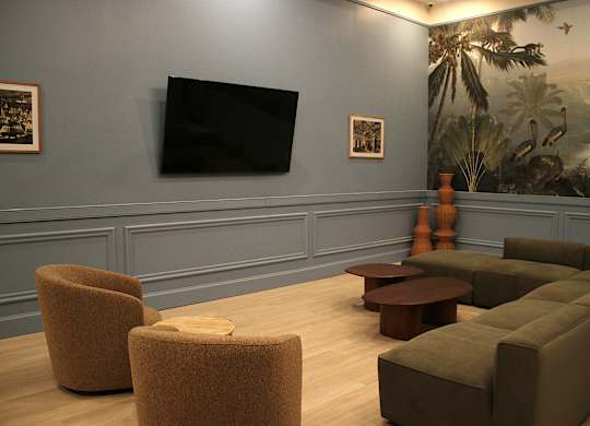 A room with a large painting of a jungle scene on the wall and a flat screen TV mounted above a sofa.