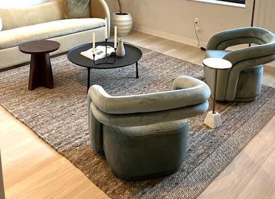 A living room with a white couch, a grey armchair, a small table with a plant on it, and a large window.