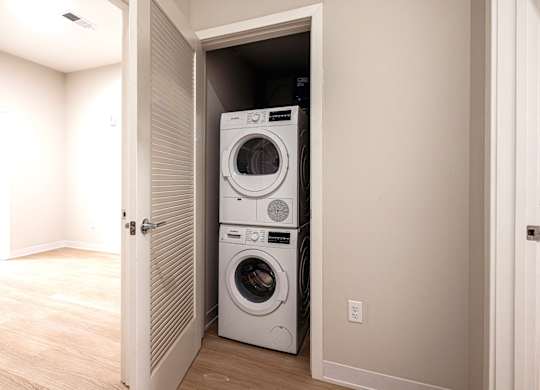 A white dryer and washer are stacked on top of each other in a small, white-walled laundry room.