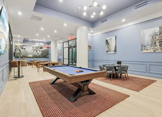 A pool table is in the middle of a room with a blue wall and a painting of a cityscape. at LiveWell Apartments, Pittsburgh