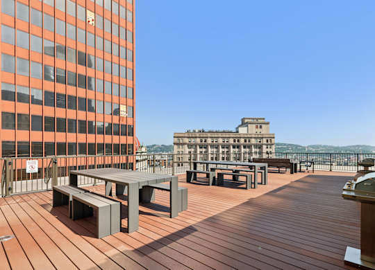 A wooden deck with benches and a table with a building in the background. at LiveWell Apartments, Pittsburgh, PA