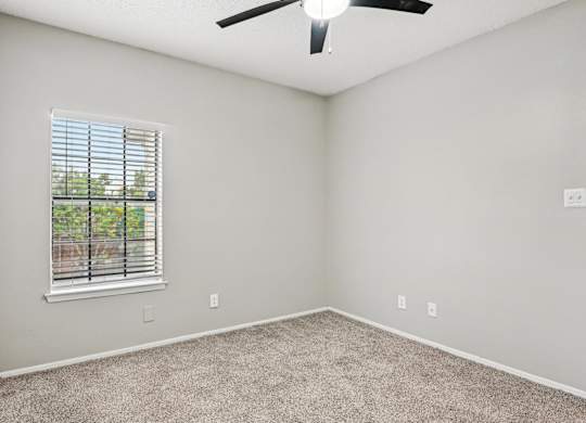 A room with a ceiling fan and a window with blinds.