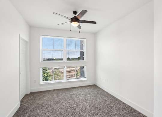 A room with a ceiling fan and a window overlooking a building.