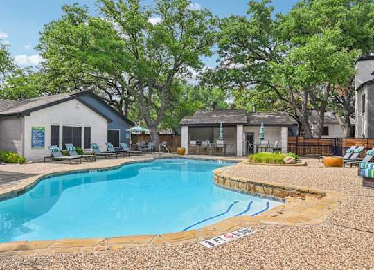 A pool surrounded by trees and chairs.