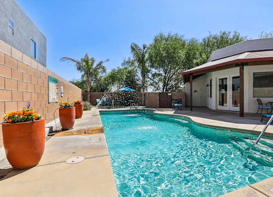A pool with a waterfall and a patio area with chairs.