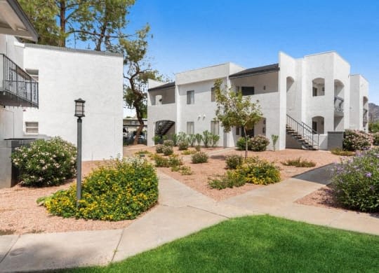 a group of white apartment buildings with a sidewalk and grass at Vertu, Phoenix, AZ