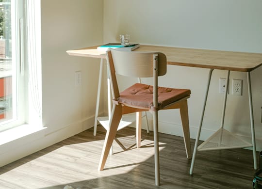 A room with a desk, chair and a vase with a flower.