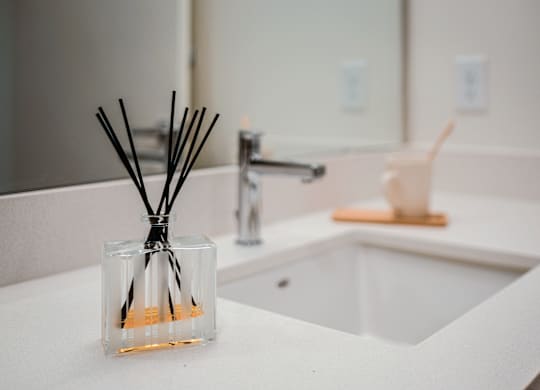 A glass container with reed sticks sits on a white countertop.