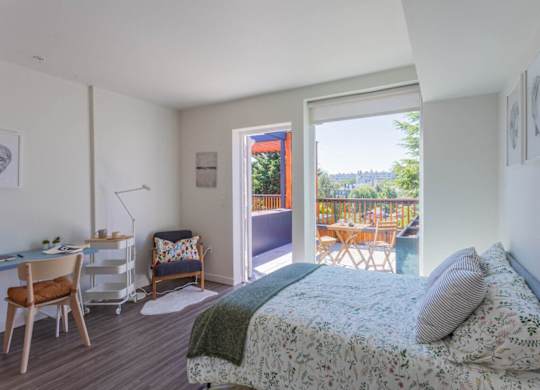 A bedroom with a bed, desk, chair, and a view of the backyard through the open door.