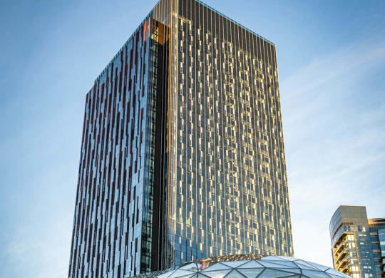 a tall skyscraper towering over a city with a glass dome in the foreground