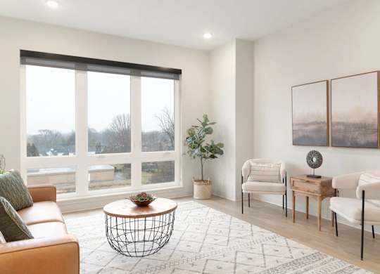 A living room with a large window, a sofa, a coffee table, and a potted plant.