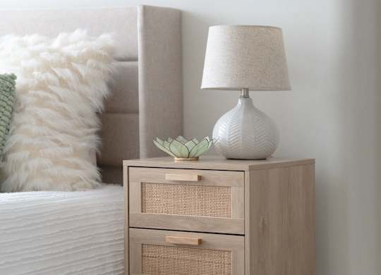 A white lamp with a green plant on a wooden nightstand.