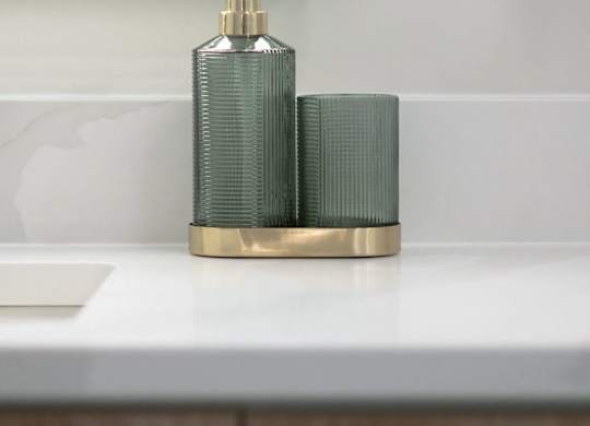 A gold soap dispenser with a green pump sits on a white countertop.