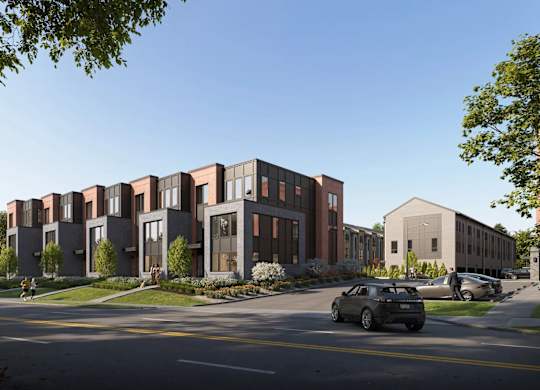 A modern building with a red brick facade is surrounded by greenery and parked cars.