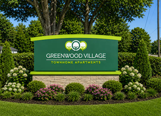 A sign for Greenwood Village Townhome Apartments is surrounded by a flower bed.