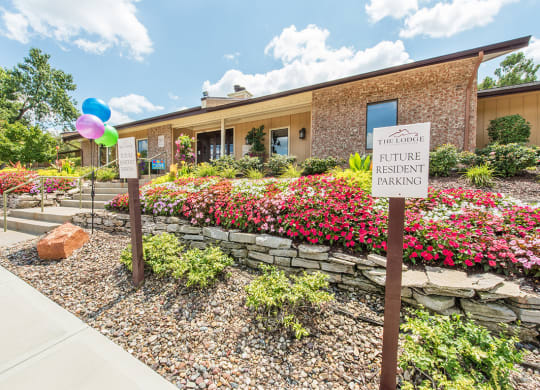 a building with a sign in front of a flower garden at Lodge of Overland Park Apartments, Overland Park , KS 66212
