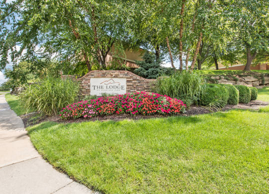 a sign for the home is in front of a sidewalk and flowers at Lodge of Overland Park Apartments, Kansas