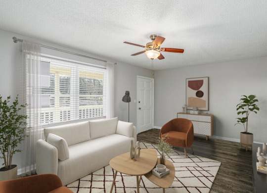 A living room with a white couch, a brown chair, a coffee table, and a ceiling fan.