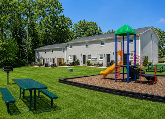 A playground with a green slide and a picnic table in front of a grey building.