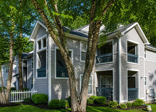 A two-story house with a white picket fence and trees in front.