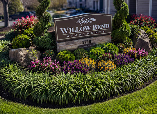A sign that says Willow Bend in front of a flower bed.