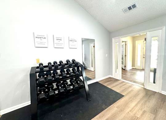 A black dumbbell rack is in the corner of a room with a mirror and three signs on the wall.