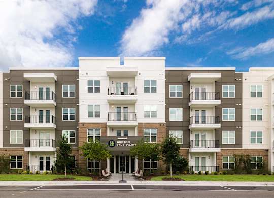 A large apartment complex with a green lawn in front at Hudson at Renaissance Apartments, Wilmington 28405