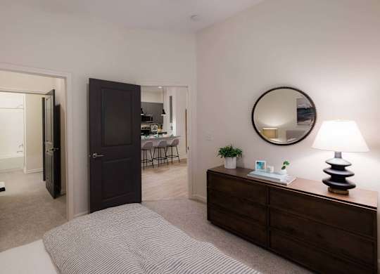 A bedroom with a bed, dresser, mirror, and lamp at Hudson at Renaissance Apartments, North Carolina 28405