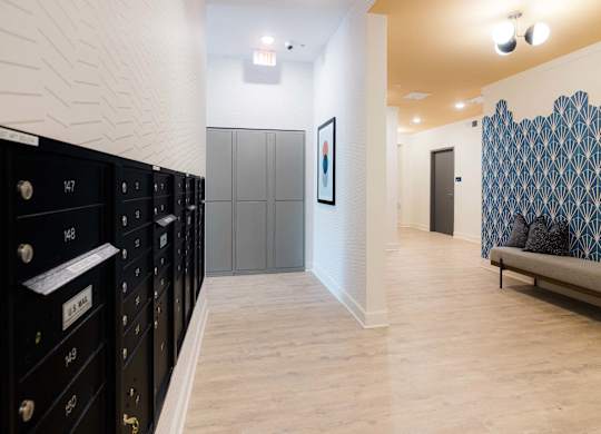A hallway with a row of black lockers on the left and a bench with a blue and white patterned wall behind it on the right at Hudson at Renaissance Apartments, Wilmington