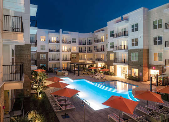 A swimming pool surrounded by orange umbrellas and chairs in a courtyard at night at Hudson at Renaissance Apartments, Wilmington