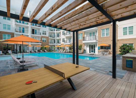 A red paddle is on a wooden table in the foreground of a pool area at Hudson at Renaissance Apartments, Wilmington, North Carolina