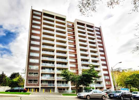 A tall apartment building with a parking lot in front.
