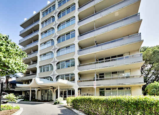 A large white apartment building with balconies and a covered walkway.