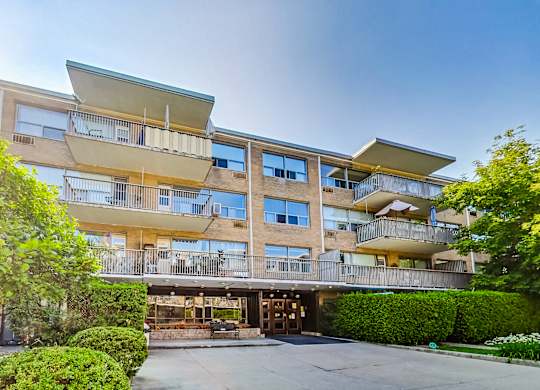 an apartment building with a sidewalk and trees in front of it