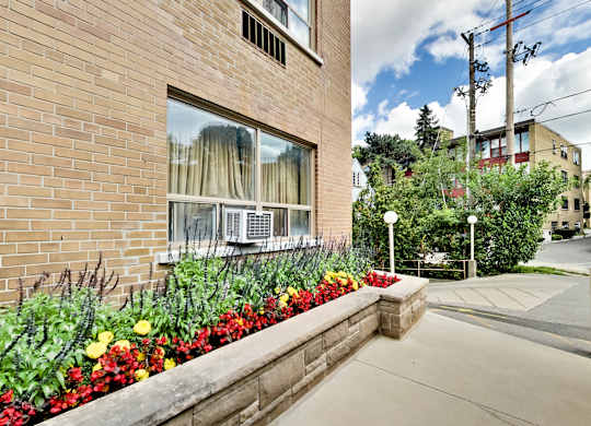 a side view of a brick building with a flower garden on the sidewalk