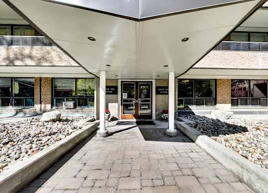 the front entrance of a building with a brick walkway and a rock garden