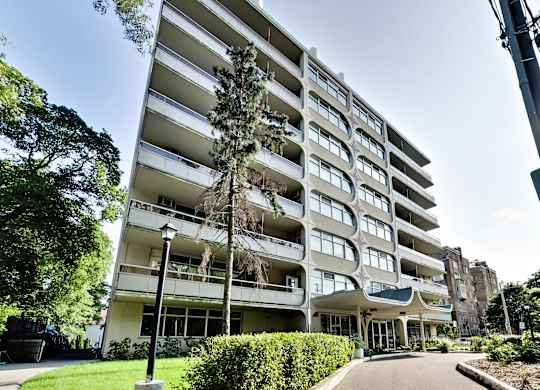 A tall white apartment building with balconies and a green lawn in front.