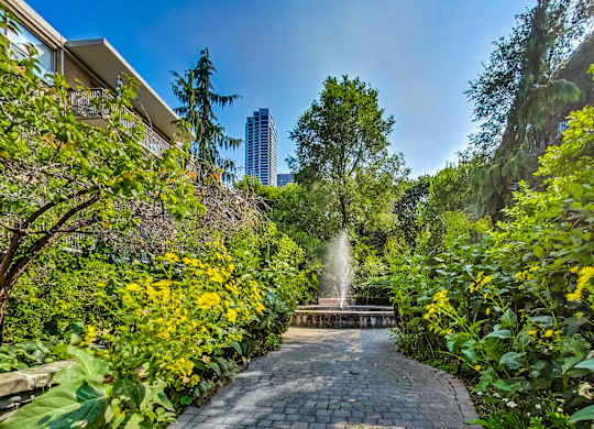 a fountain in the middle of a park with trees and flowers