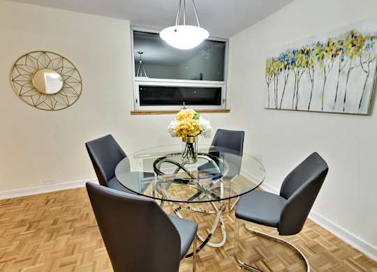 A glass dining table with four chairs and a flower vase on top.