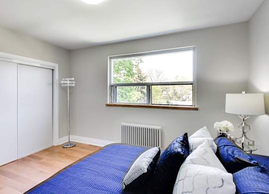 A bedroom with a bed, pillows, a lamp, and a window.