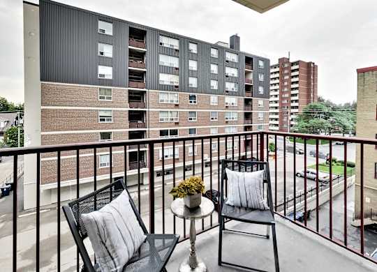 an apartment balcony with two chairs and a table with flowers