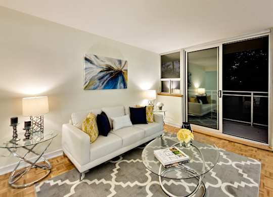 A living room with a white couch, a glass coffee table, and a painting on the wall.