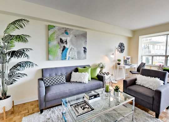 A living room with a grey couch, a glass coffee table, and a large painting on the wall.
