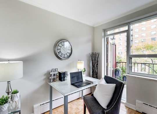 a living room with a desk with a laptop and a clock on the wall