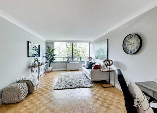 A living room with a white couch, a grey rug, and a clock on the wall.