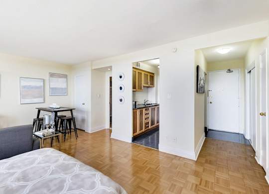 A bedroom with a bed, a table and chairs, and a kitchen area.